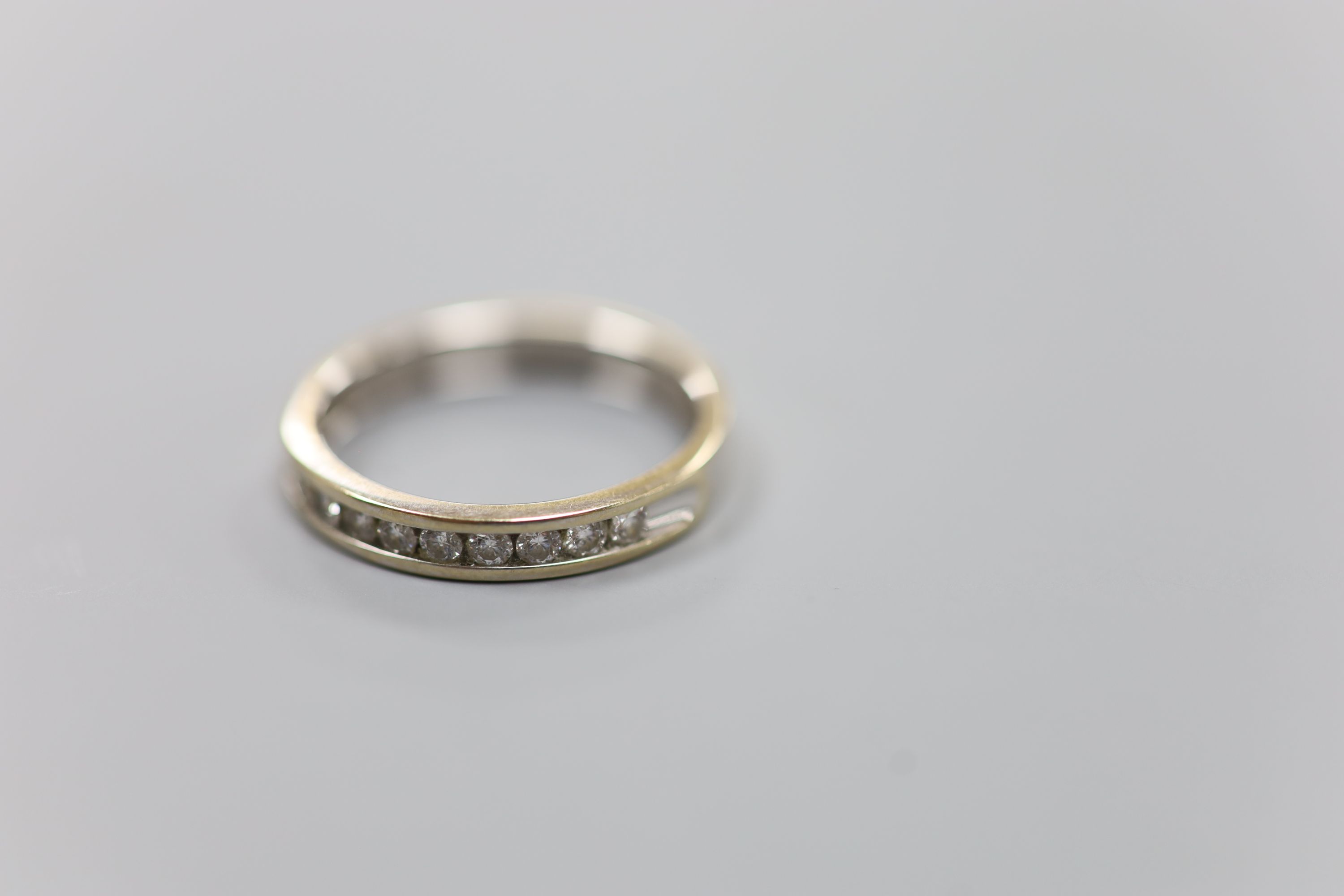 A modern 18ct white gold (worn) and nine stone channel set diamond half eternity ring, size P